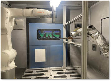 Inside of chamber with a spray nozzle on the right side and a 5-axis robotic arm on the left.